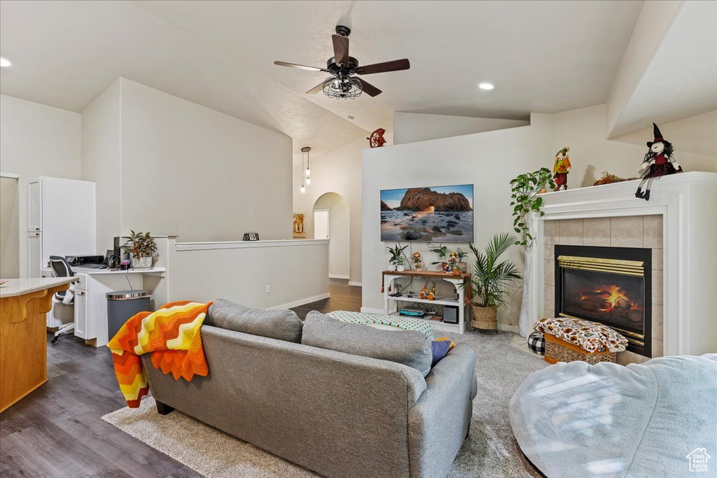 Living room featuring dark hardwood / wood-style floors, vaulted ceiling, a tiled fireplace, and ceiling fan