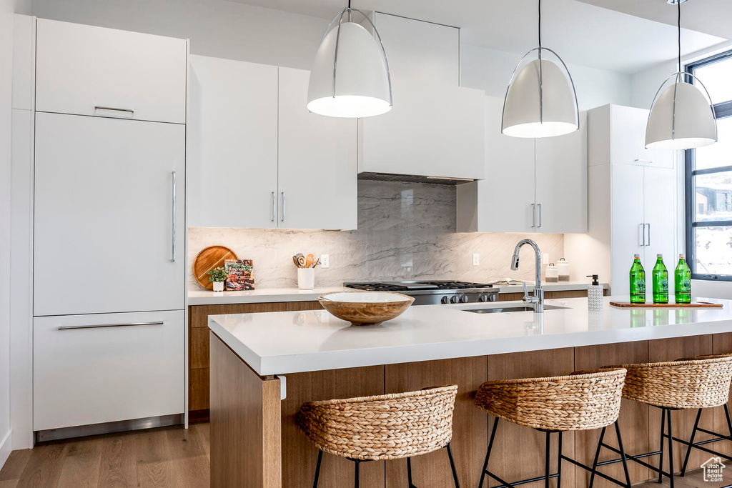 Kitchen featuring hardwood / wood-style floors, an island with sink, sink, hanging light fixtures, and white cabinets