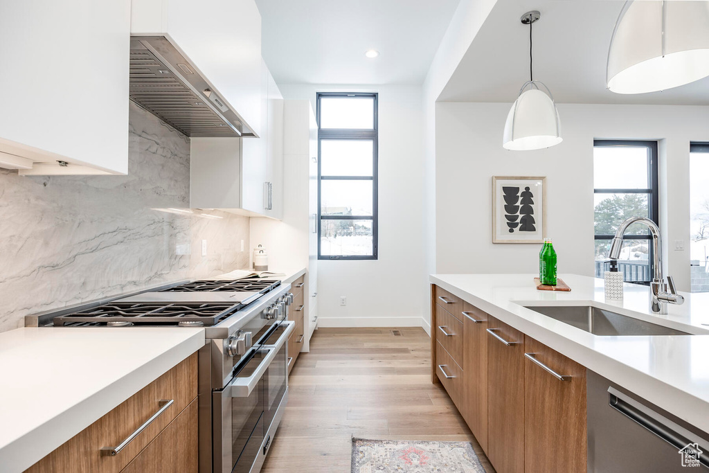 Kitchen featuring a healthy amount of sunlight, stainless steel appliances, decorative light fixtures, and wall chimney range hood