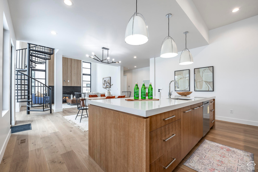 Kitchen featuring light hardwood / wood-style floors, a large island with sink, sink, and hanging light fixtures