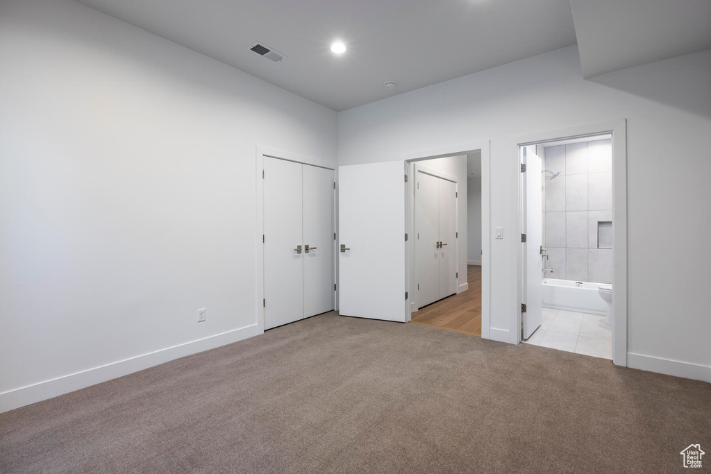 Unfurnished bedroom featuring ensuite bath, light colored carpet, and a closet