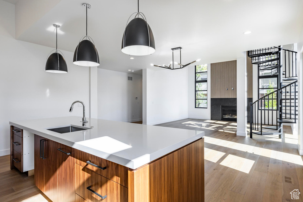 Kitchen with light wood-type flooring, pendant lighting, a tiled fireplace, sink, and a center island with sink