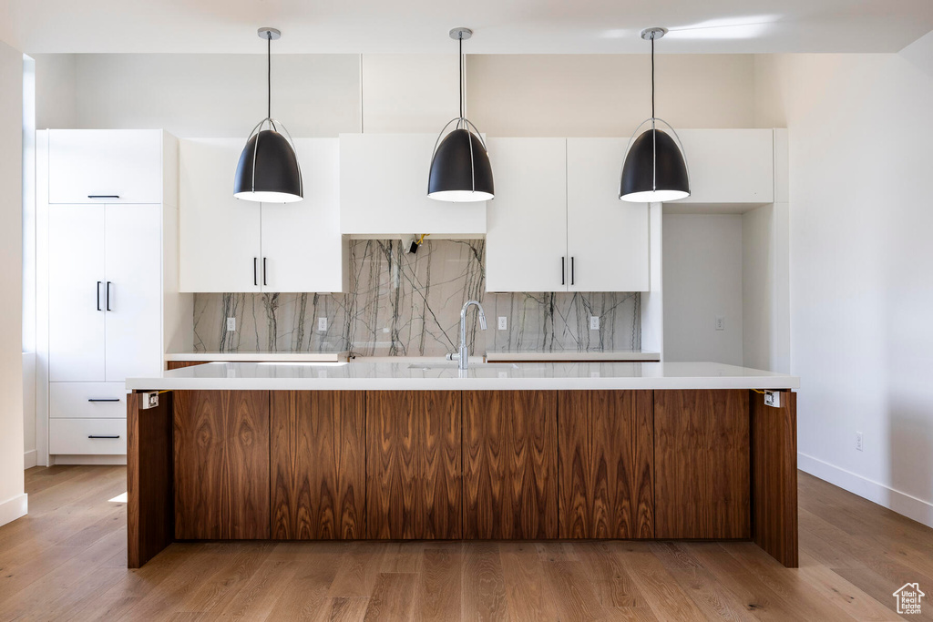 Kitchen featuring a center island, decorative backsplash, light hardwood / wood-style floors, and white cabinetry