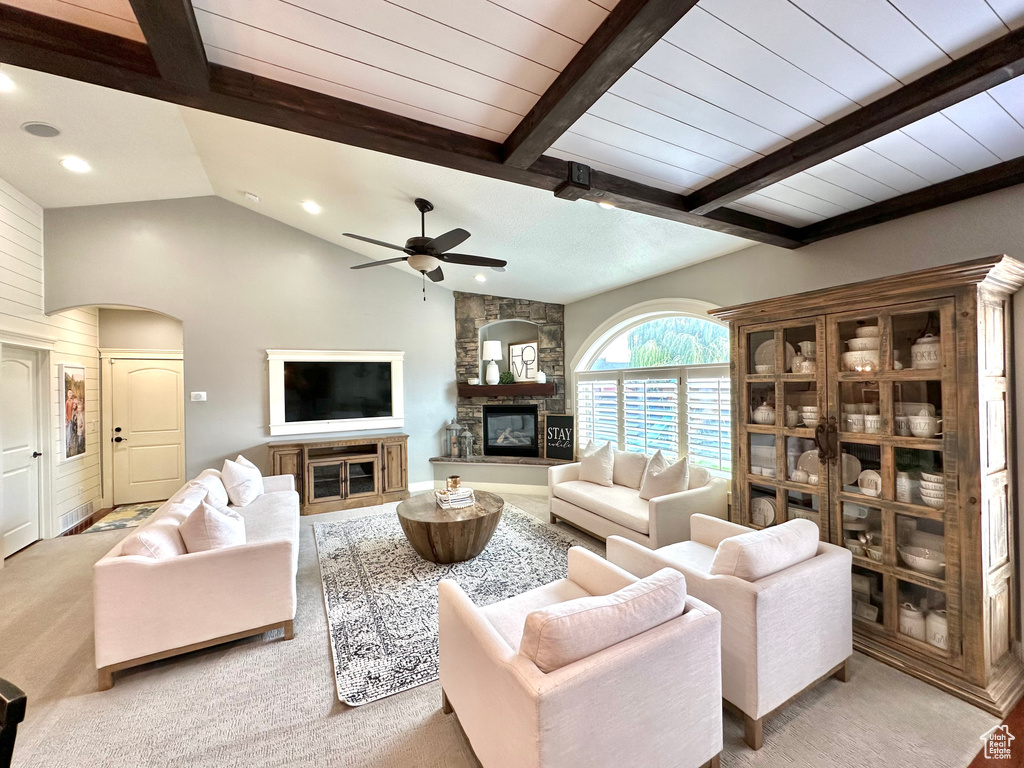 Living room featuring lofted ceiling with beams, wood walls, light colored carpet, a stone fireplace, and ceiling fan