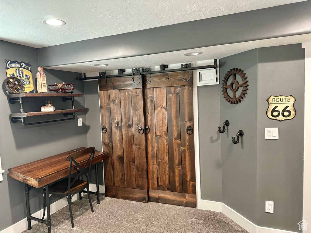 Carpeted home office with a barn door and a textured ceiling