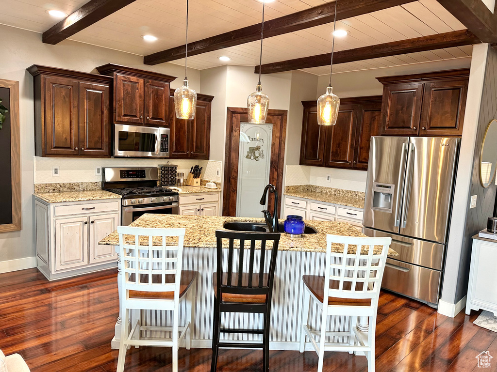 Kitchen featuring a breakfast bar, beamed ceiling, stainless steel appliances, a center island with sink, and dark hardwood / wood-style floors