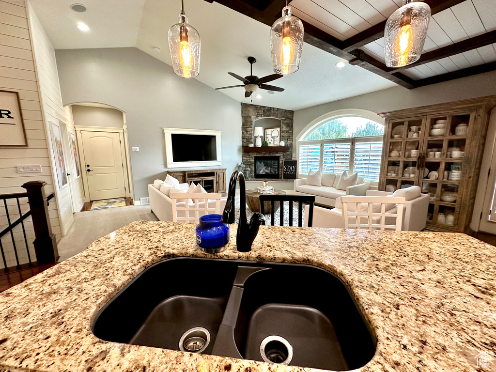 Kitchen with ceiling fan, light stone counters, sink, a fireplace, and vaulted ceiling