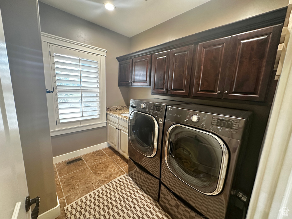 Clothes washing area with dark tile patterned floors, cabinets, and washing machine and clothes dryer