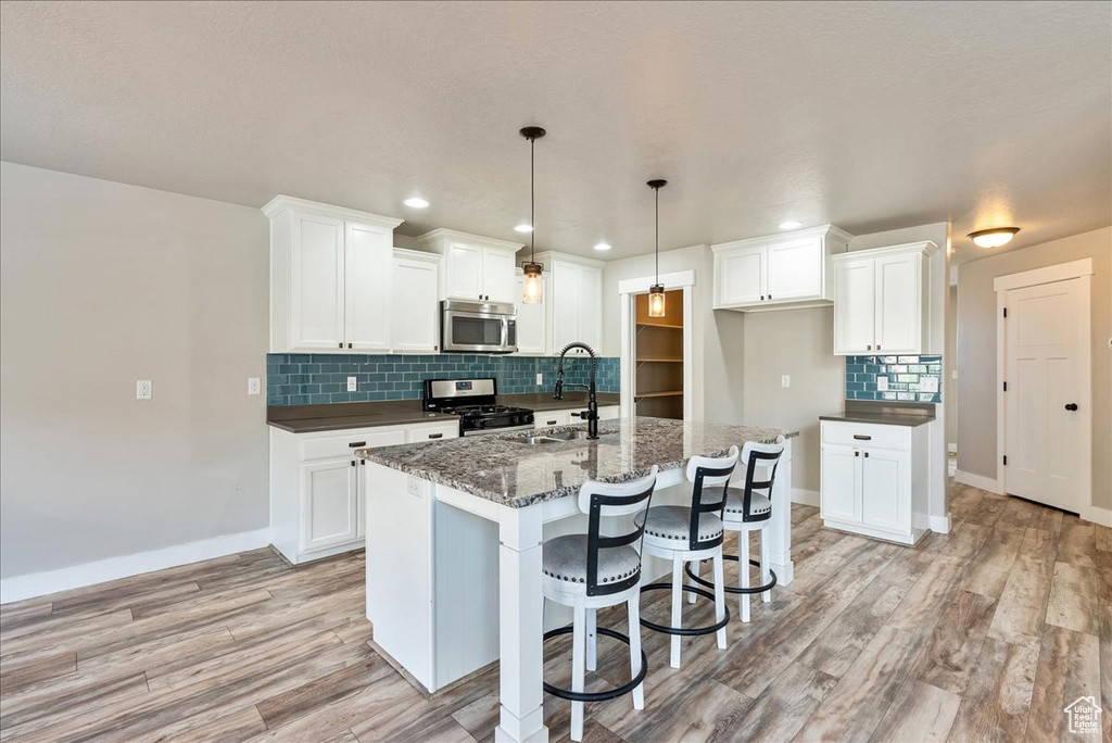 Kitchen with a kitchen island with sink, appliances with stainless steel finishes, light hardwood / wood-style floors, and white cabinetry