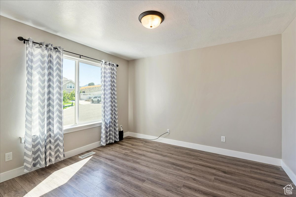 Empty room with a textured ceiling and hardwood / wood-style floors