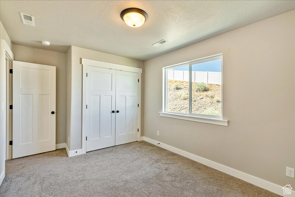 Unfurnished bedroom with a textured ceiling, light carpet, and a closet