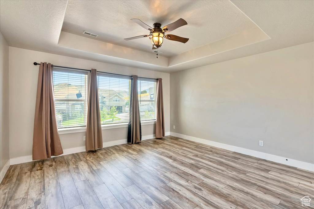 Empty room featuring light wood-type flooring, a textured ceiling, a tray ceiling, and ceiling fan