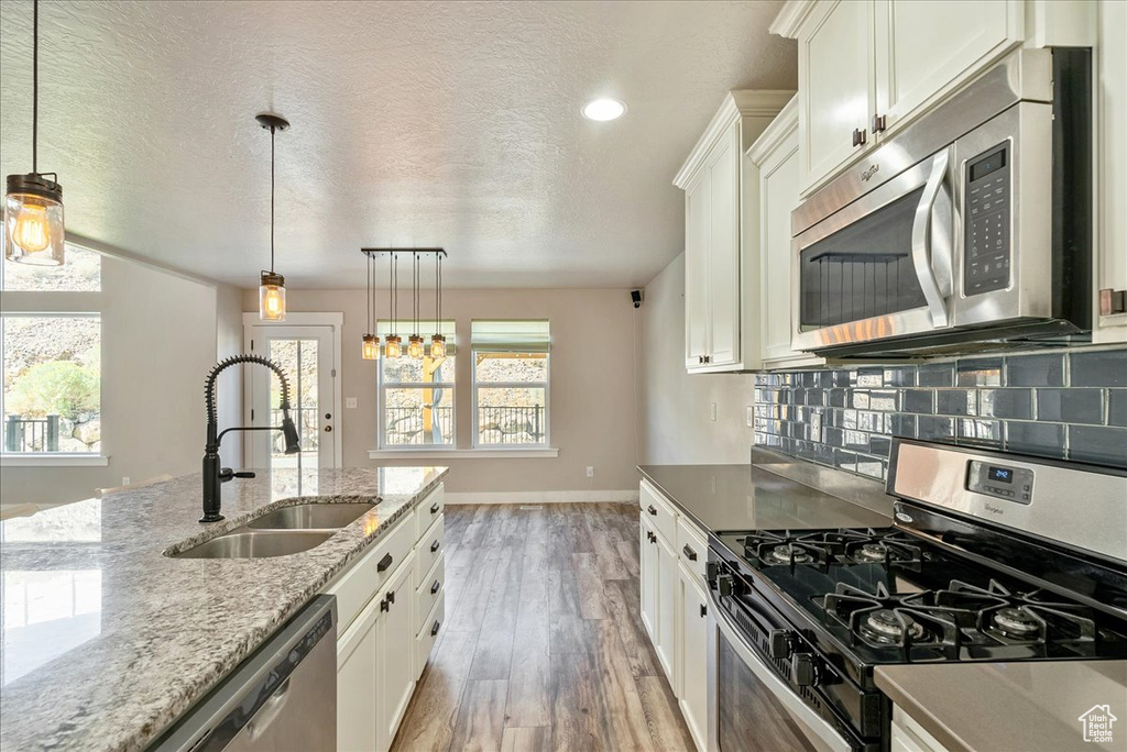 Kitchen with hanging light fixtures, white cabinets, stainless steel appliances, hardwood / wood-style flooring, and sink