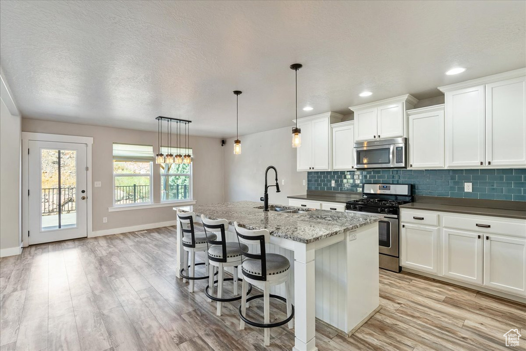 Kitchen with hanging light fixtures, stainless steel appliances, light wood-type flooring, a center island with sink, and sink