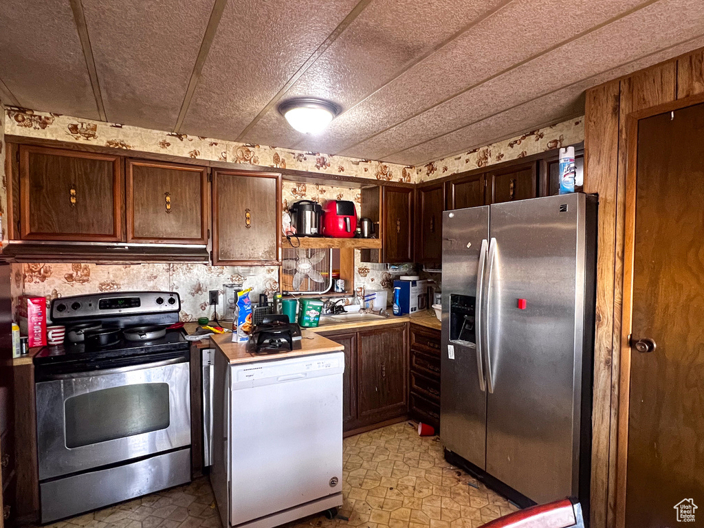 Kitchen featuring a textured ceiling, dark brown cabinetry, sink, and stainless steel appliances