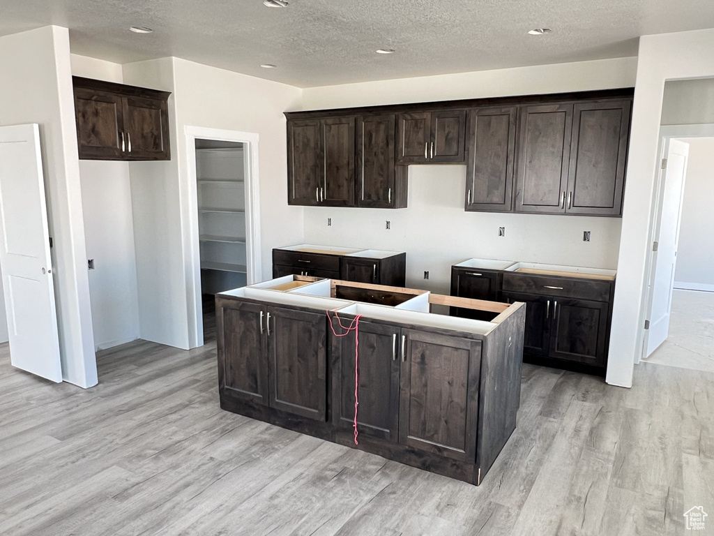 Kitchen featuring a textured ceiling, a center island, and dark brown cabinetry