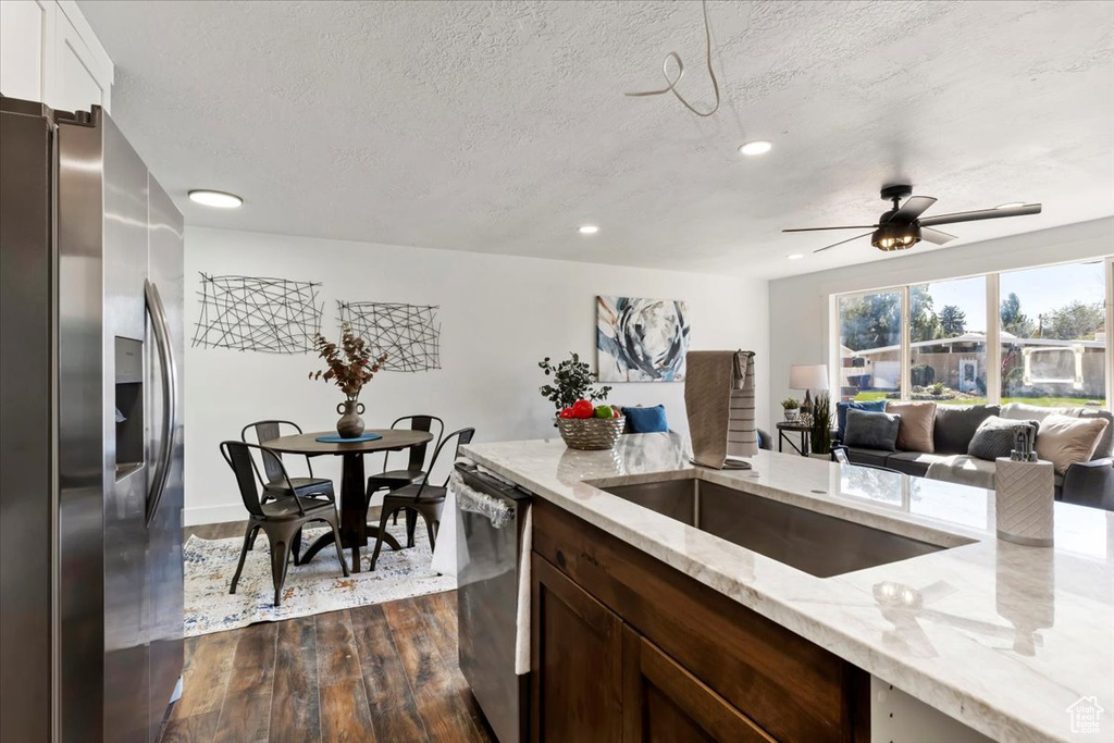 Kitchen with light stone countertops, ceiling fan, appliances with stainless steel finishes, and dark hardwood / wood-style flooring