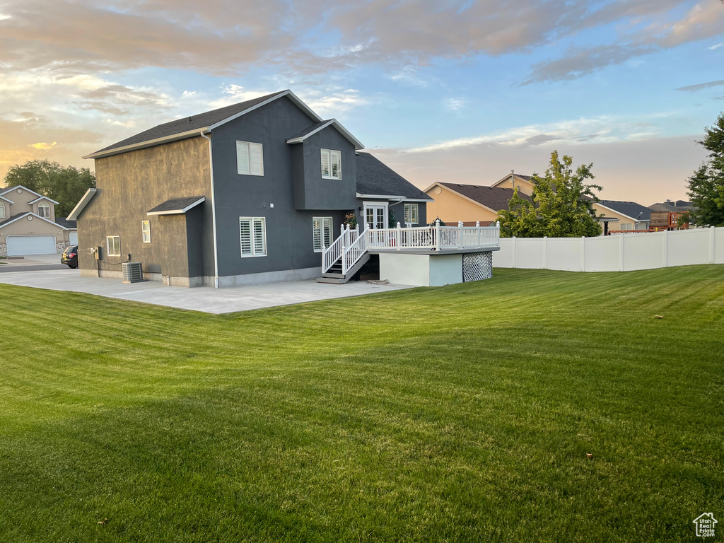 Back house at dusk featuring a garage, a deck, a yard, and a patio area