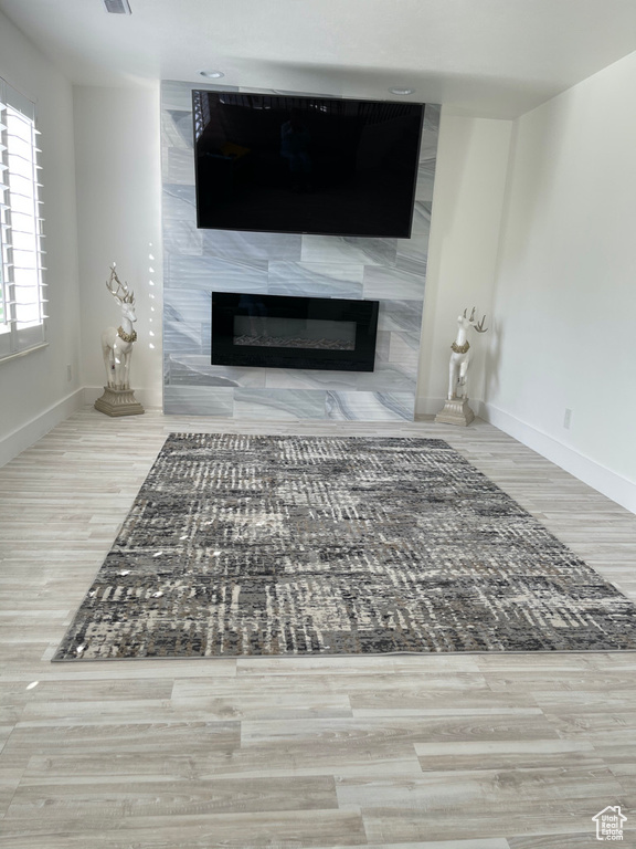 Unfurnished living room with a tiled fireplace and light hardwood / wood-style flooring