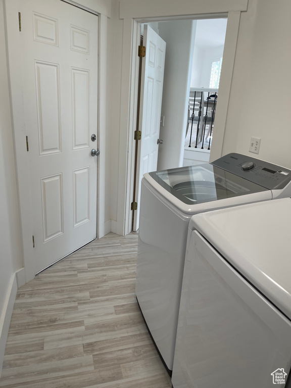 Clothes washing area with light wood-type flooring and washer and clothes dryer