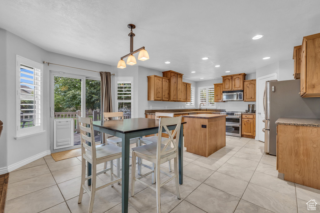 Kitchen with appliances with stainless steel finishes, a kitchen island, light tile patterned floors, and decorative light fixtures