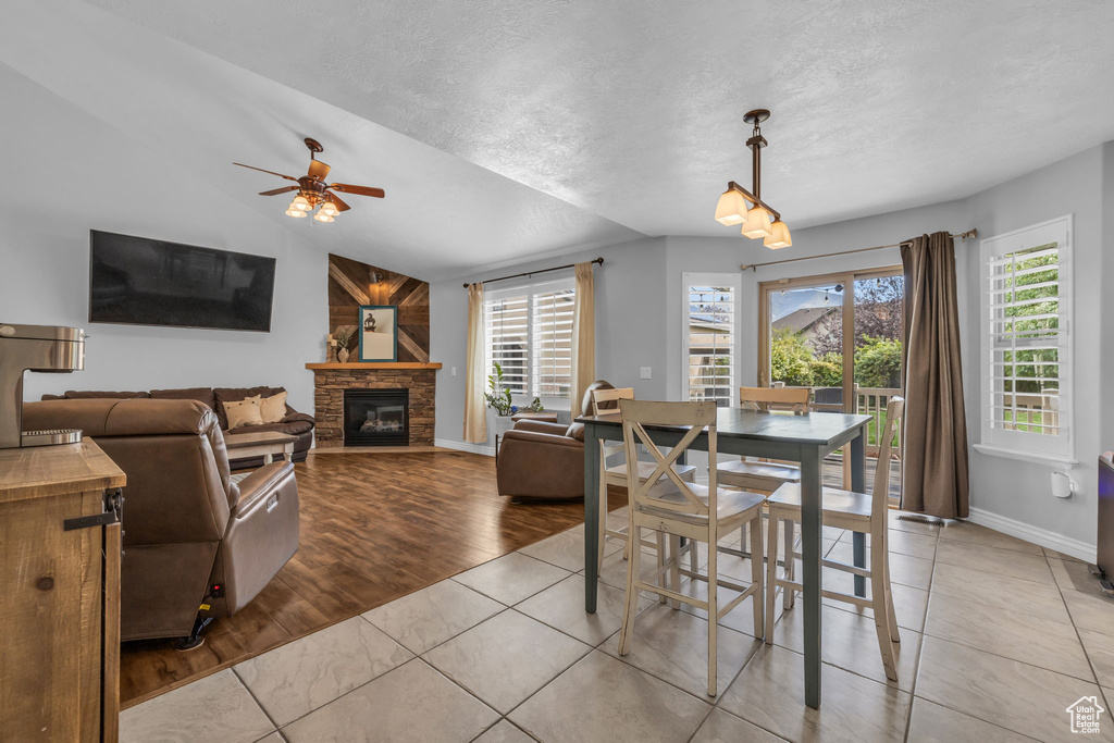 Dining area with a textured ceiling, vaulted ceiling, a fireplace, light hardwood / wood-style flooring, and ceiling fan