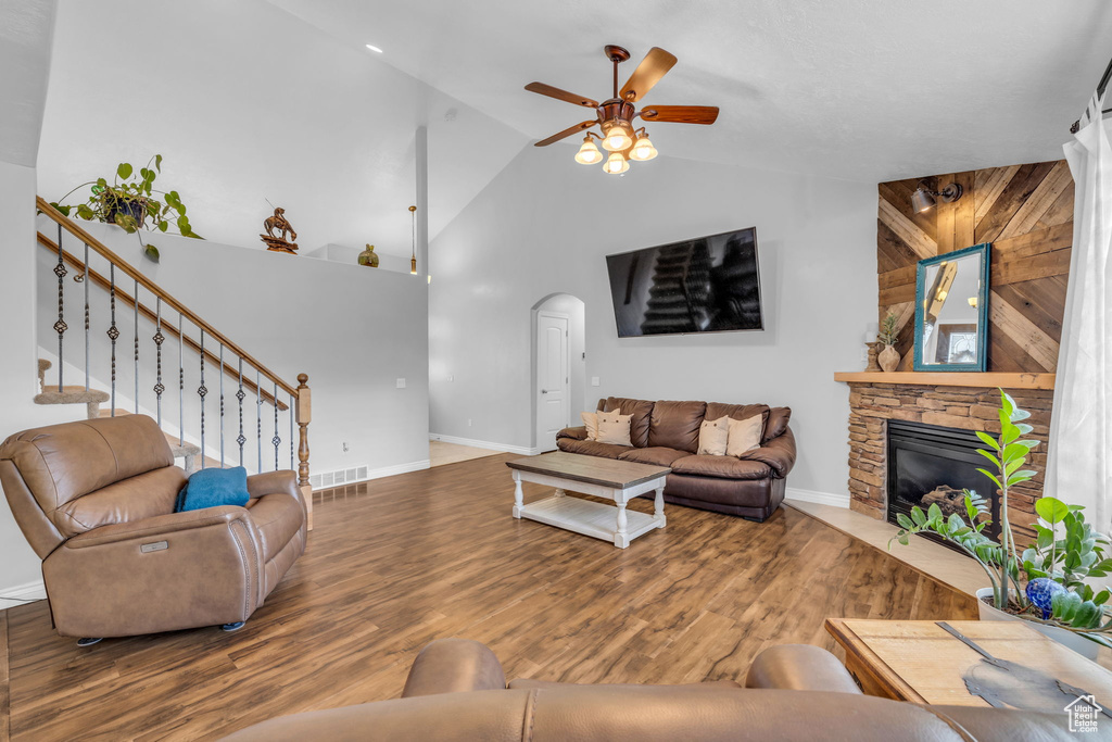 Living room with high vaulted ceiling, wooden walls, hardwood / wood-style floors, a stone fireplace, and ceiling fan