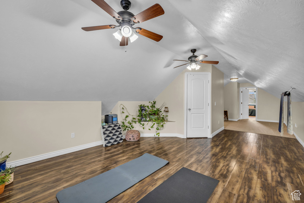 Workout area with ceiling fan, vaulted ceiling, and dark hardwood / wood-style flooring