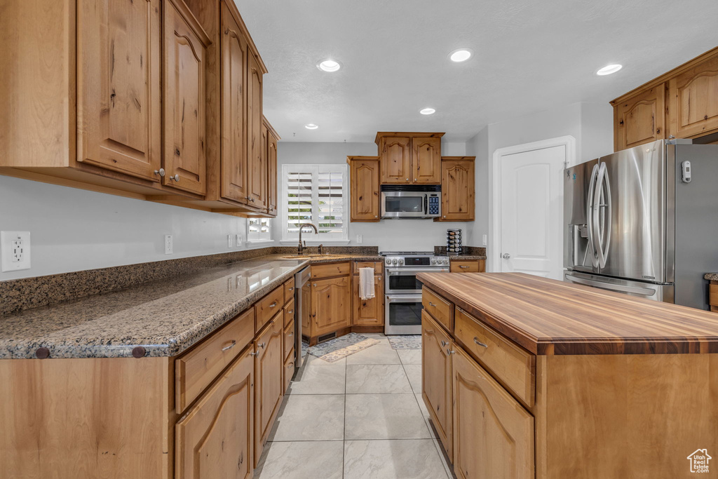 Kitchen with appliances with stainless steel finishes, dark stone countertops, a kitchen island, and sink