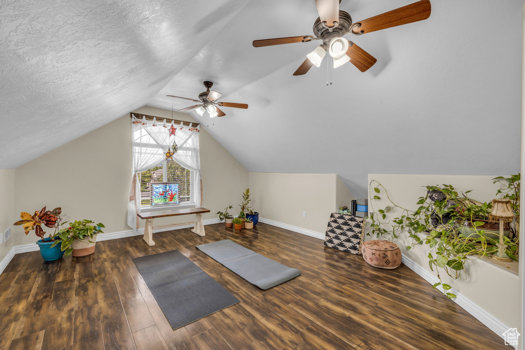 Exercise room with lofted ceiling, ceiling fan, dark hardwood / wood-style floors, and a textured ceiling