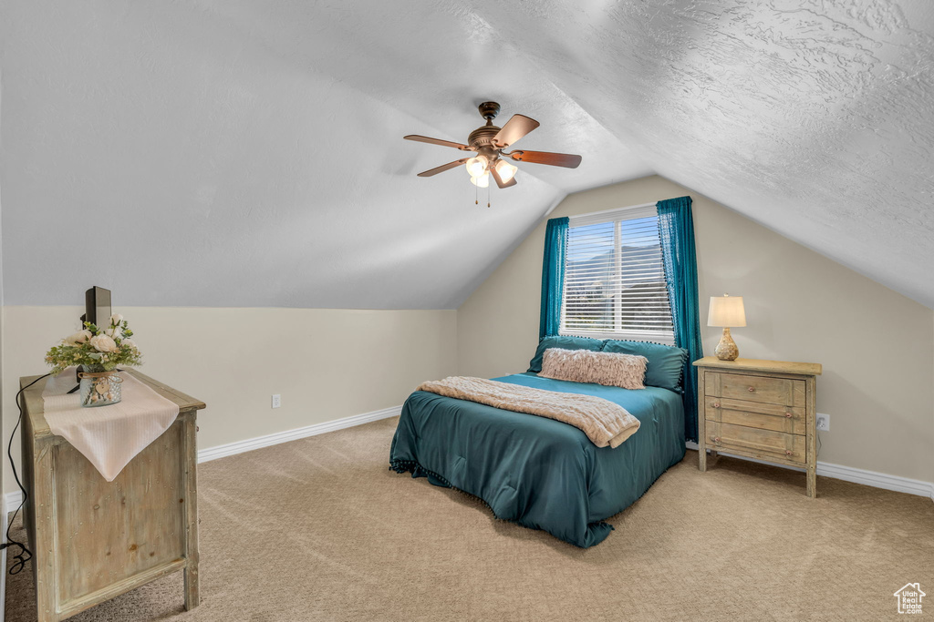 Bedroom with a textured ceiling, carpet flooring, vaulted ceiling, and ceiling fan