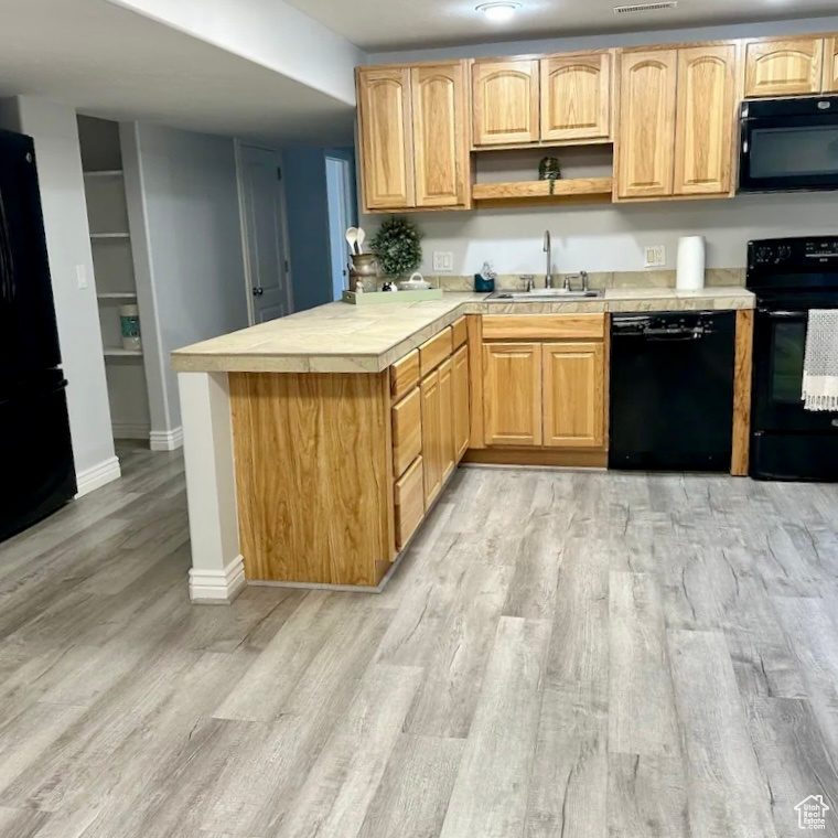 Kitchen featuring light wood-type flooring, black appliances, kitchen peninsula, and sink