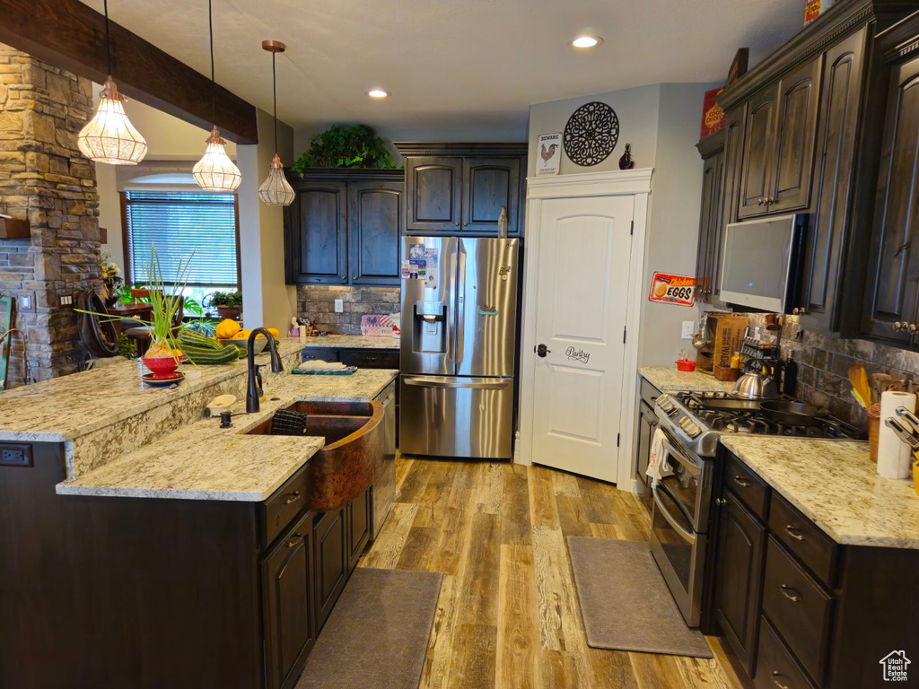 Kitchen featuring appliances with stainless steel finishes, pendant lighting, light hardwood / wood-style flooring, dark brown cabinetry, and sink