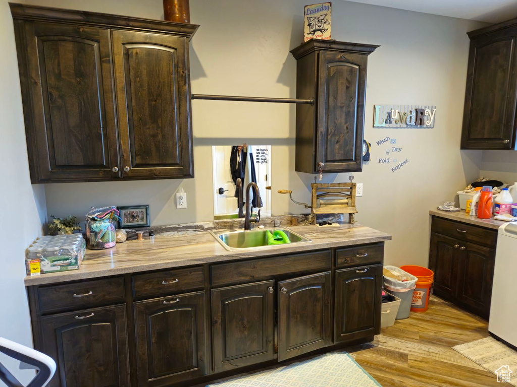 Kitchen with dark brown cabinets, light hardwood / wood-style floors, white stove, and sink