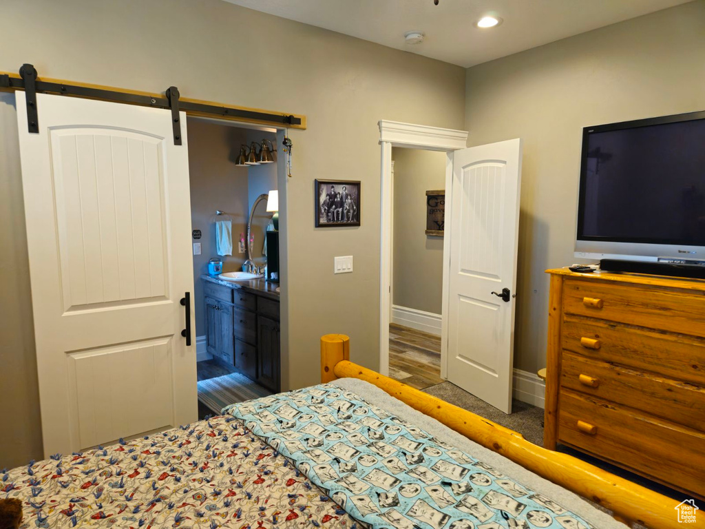 Bedroom featuring a barn door, connected bathroom, sink, and dark wood-type flooring