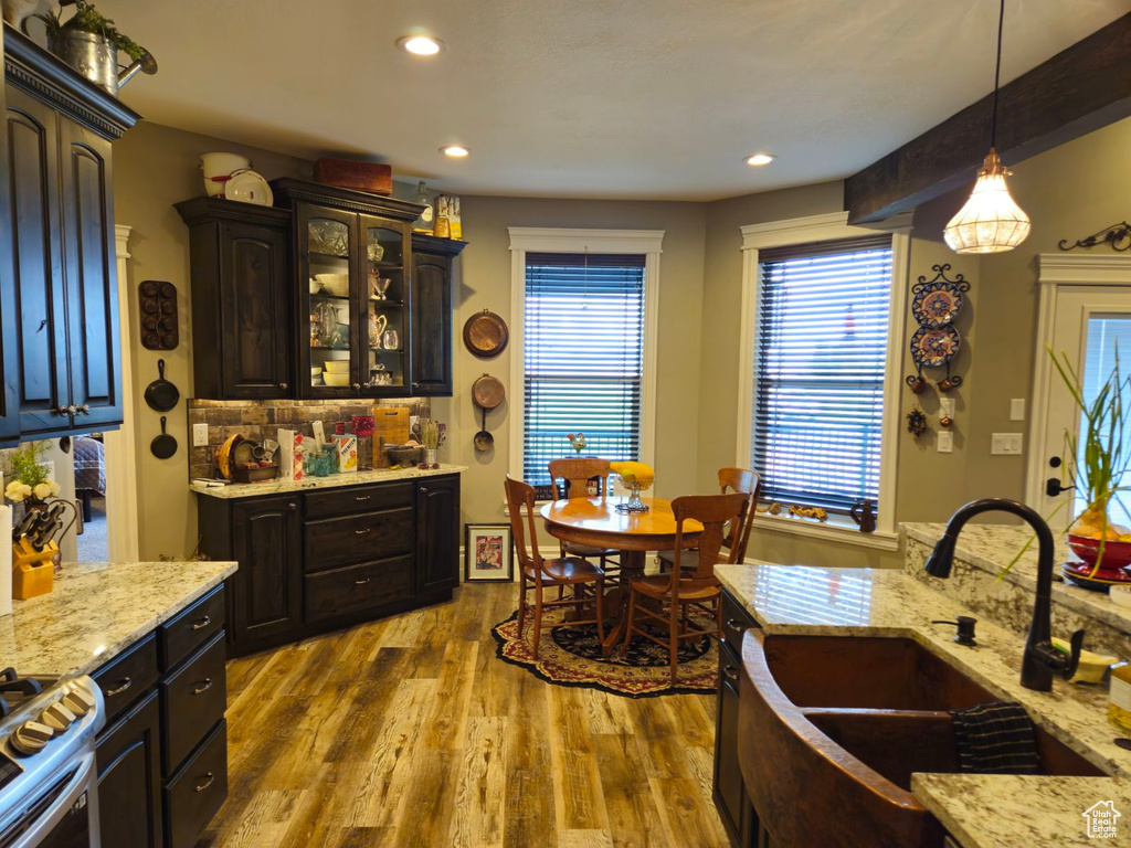 Kitchen with pendant lighting, wood-type flooring, dark brown cabinets, sink, and light stone countertops