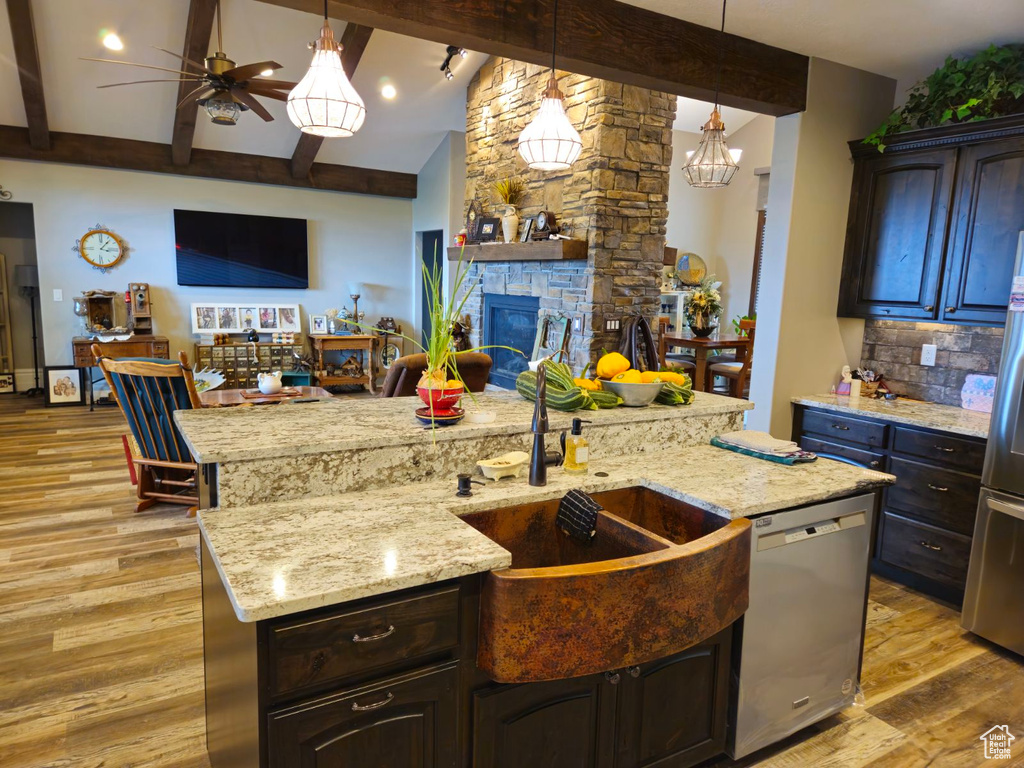 Kitchen with appliances with stainless steel finishes, a fireplace, beamed ceiling, ceiling fan, and a center island with sink