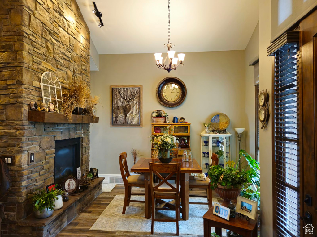 Dining room with a stone fireplace, a chandelier, dark hardwood / wood-style flooring, and rail lighting