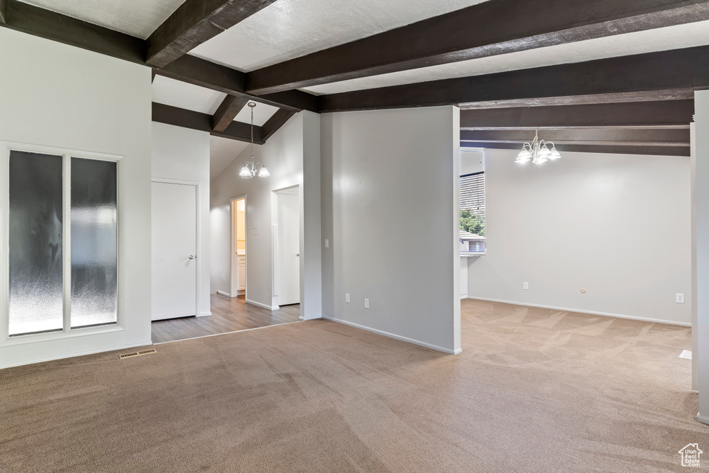 Interior space featuring a healthy amount of sunlight, lofted ceiling with beams, an inviting chandelier, and light colored carpet