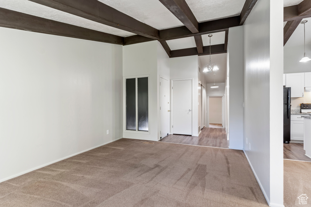 Carpeted spare room with beamed ceiling, a towering ceiling, and a notable chandelier