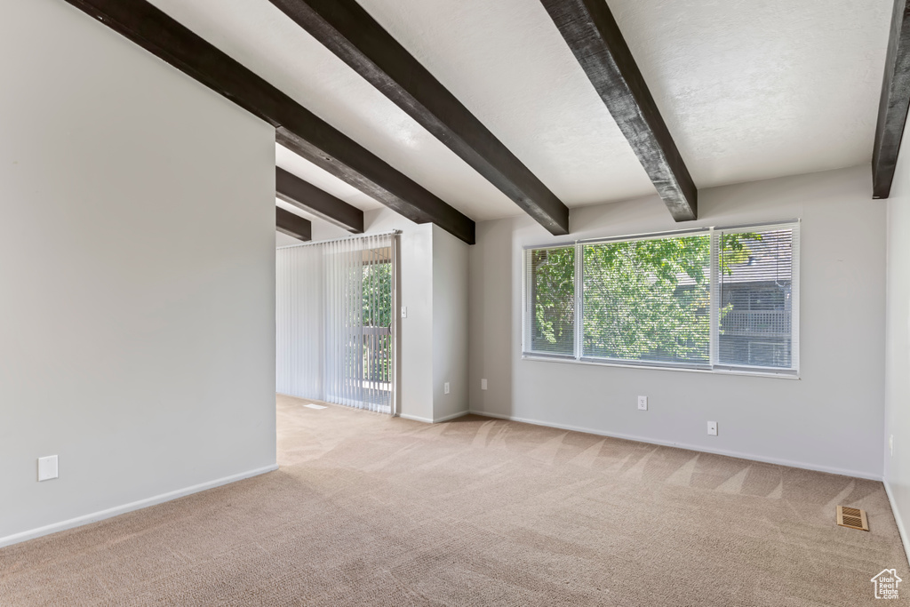 Carpeted spare room featuring beamed ceiling