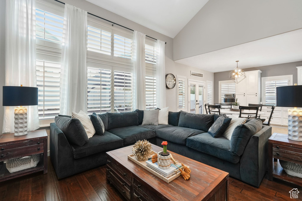 Living room with a chandelier, dark wood-type flooring, high vaulted ceiling, and a healthy amount of sunlight