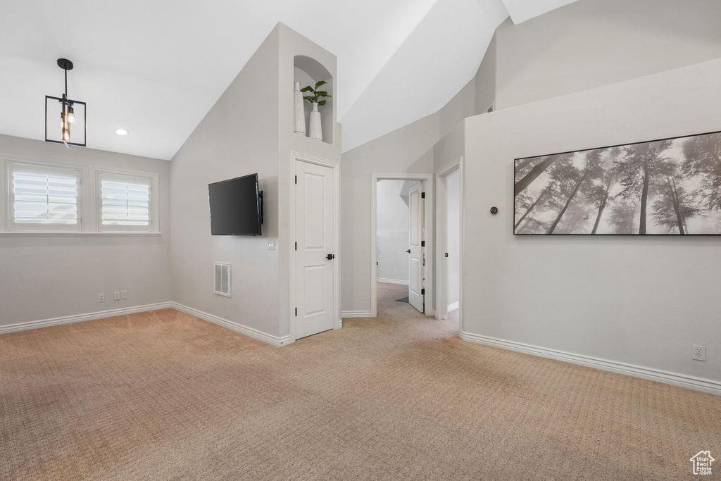 Unfurnished living room featuring light carpet, a chandelier, and high vaulted ceiling