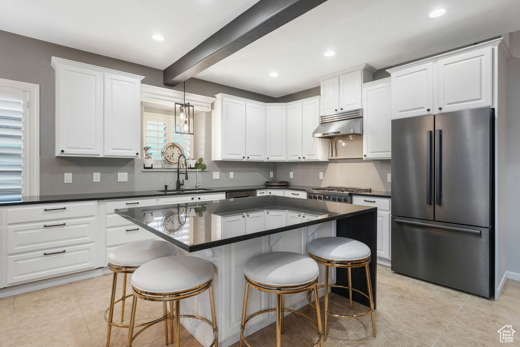 Kitchen featuring stainless steel fridge, white cabinets, a kitchen island, beam ceiling, and sink