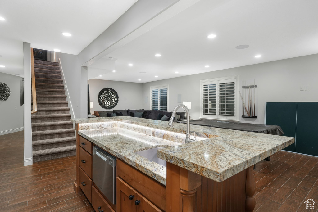 Kitchen with dishwasher, dark wood-type flooring, a kitchen island with sink, sink, and light stone countertops