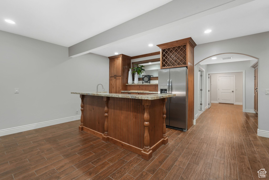 Kitchen featuring dark wood-type flooring, light stone counters, a breakfast bar, stainless steel refrigerator with ice dispenser, and sink