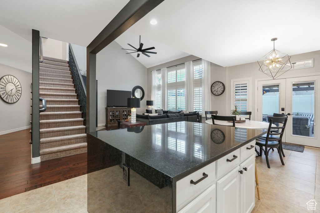 Kitchen featuring wood-type flooring, ceiling fan with notable chandelier, white cabinetry, hanging light fixtures, and a kitchen island