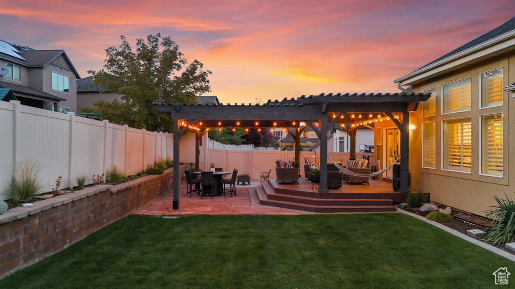 Yard at dusk with a wooden deck, a pergola, and a patio