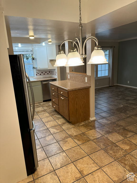 Kitchen with appliances with stainless steel finishes, hanging light fixtures, white cabinets, tasteful backsplash, and ornamental molding