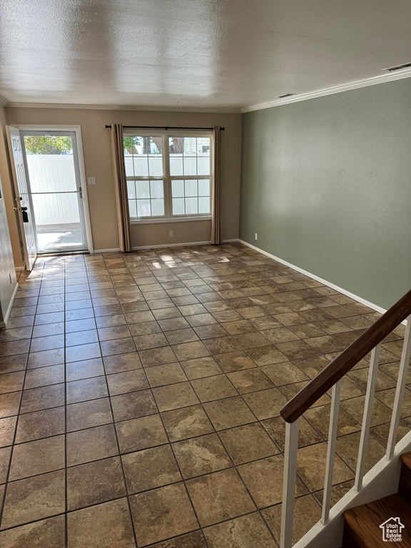 Empty room with ornamental molding, dark tile patterned flooring, and a textured ceiling